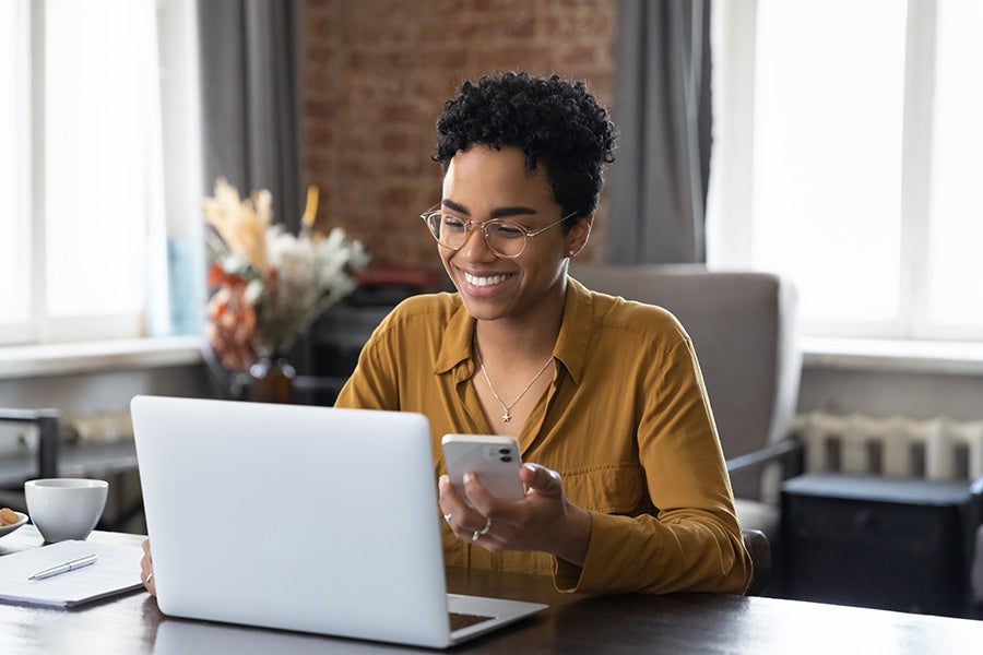 Woman looking at phone and laptop smiling